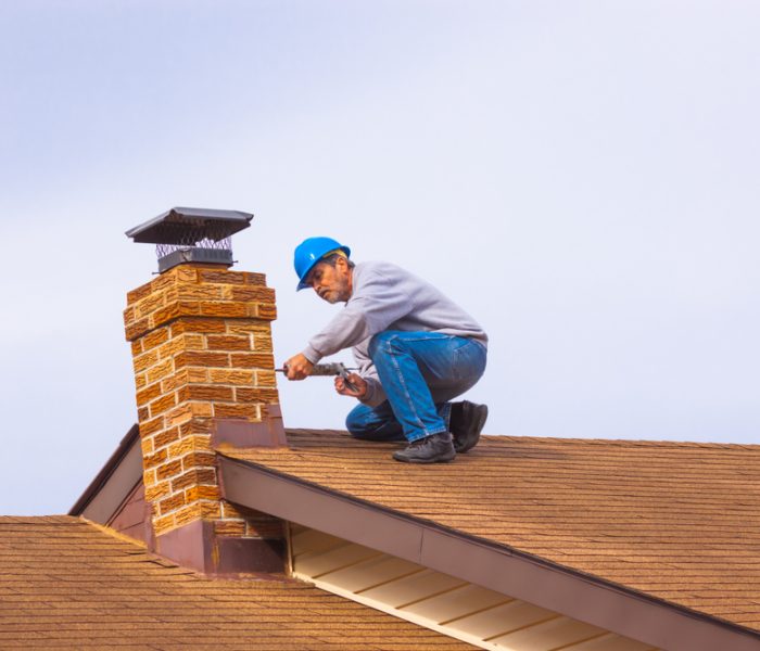 Contractor builder with blue hardhat on the roof caulking chimney